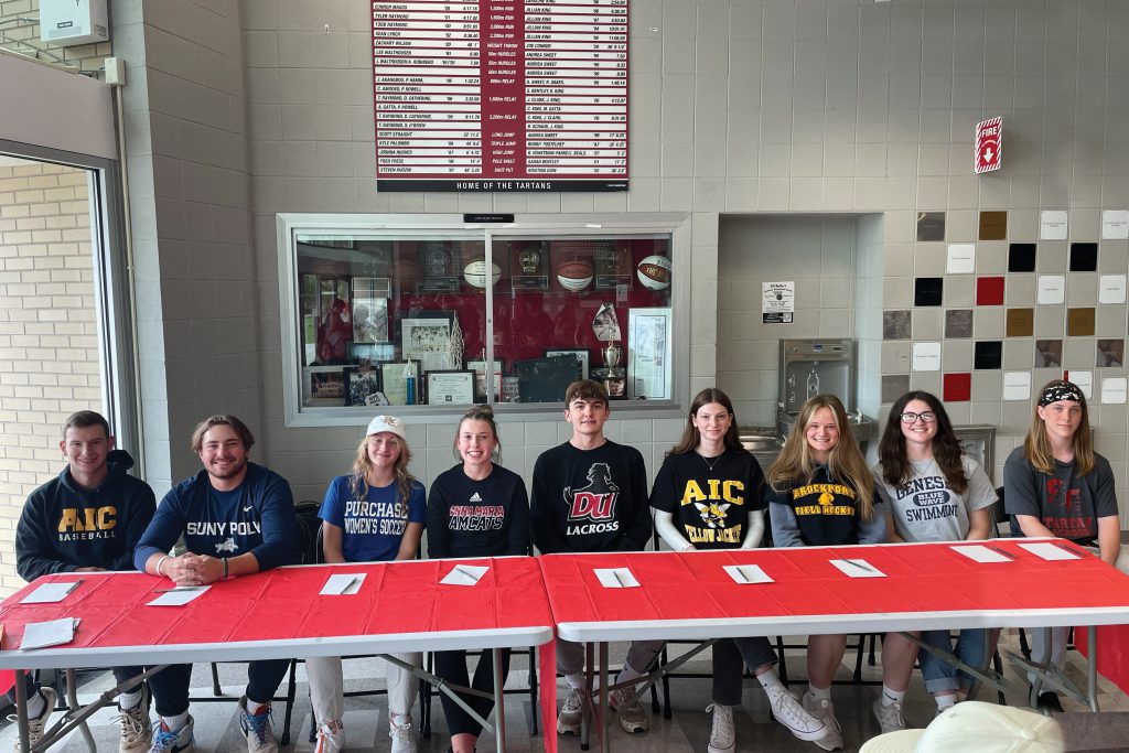 nine students sitting at a table wearing their college gear