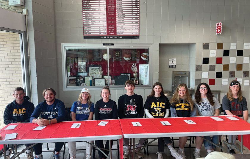 nine students sitting at a table wearing their college gear