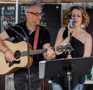 one musician plays guitar while the other one sings into a mic