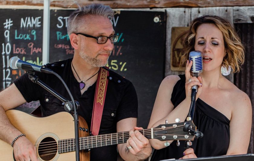 one musician plays guitar while the other one sings into a mic