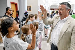 Principal stands in crowded school lobby giving high fives to students.