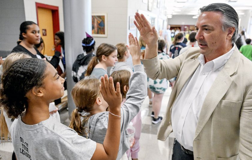 Principal stands in crowded school lobby giving high fives to students.