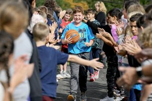 student holding a basketball is greeted by students on both sides of where he is standing. 