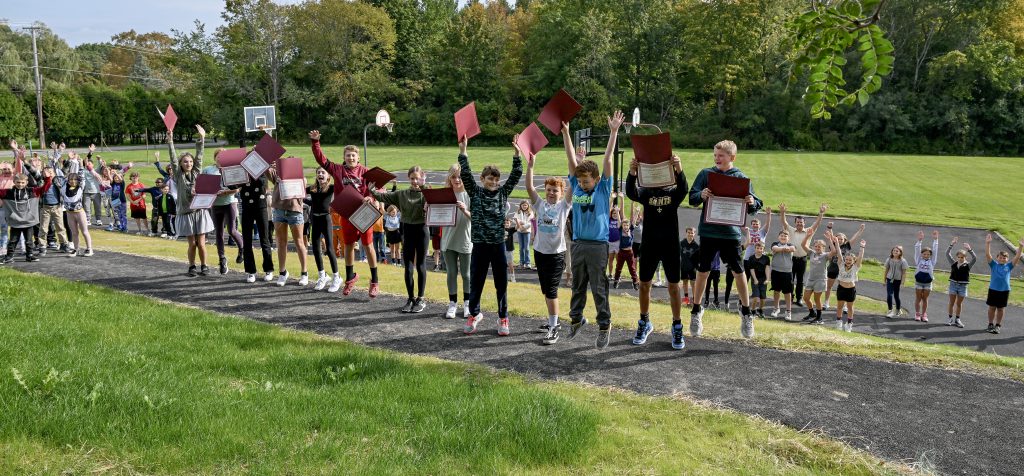 students hold up their certificates and other students hold their hands high 