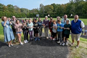 two women share a pair of large scissors to cut a ribbon with cheering students and administrators around them