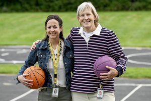 two women standing outside with their arms around each other while each holding a basketball with their other hand