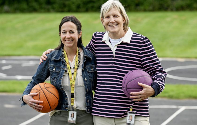 two women standing outside with their arms around each other while each holding a basketball with their other hand