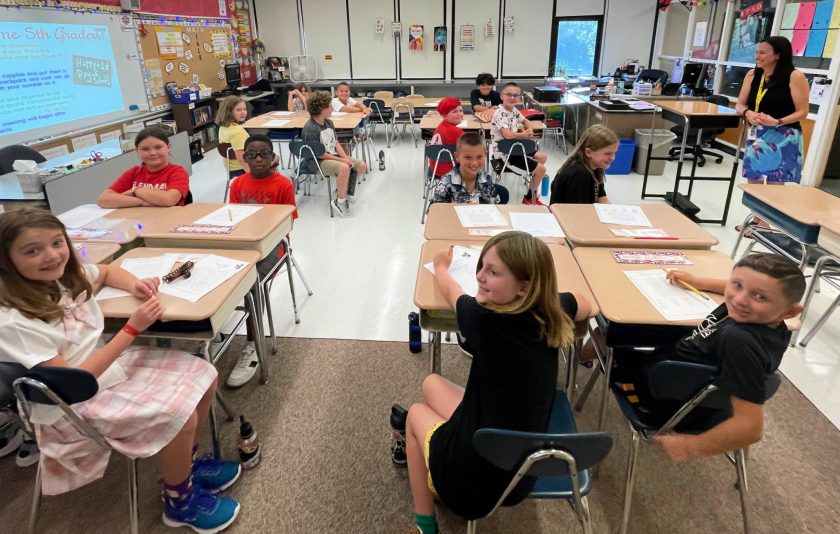 fifth graders smiling for the camera while their teacher smiles at them