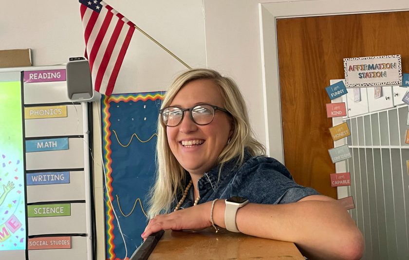 teacher standing with her arm on a shelf smiling at camera