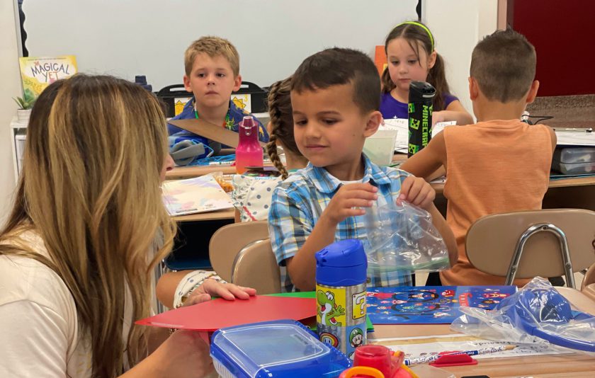 Teacher kneels to help student at desk