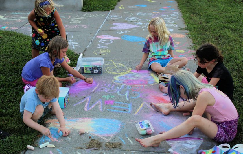 students drawing on sidewalk with chalk outside their school