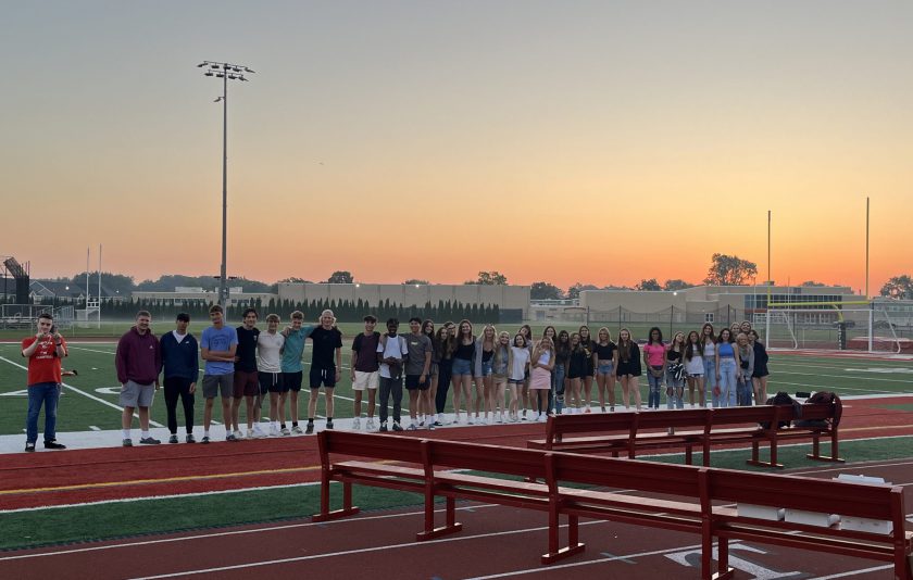 35 high school seniors standing on a track with the sunrise behind them
