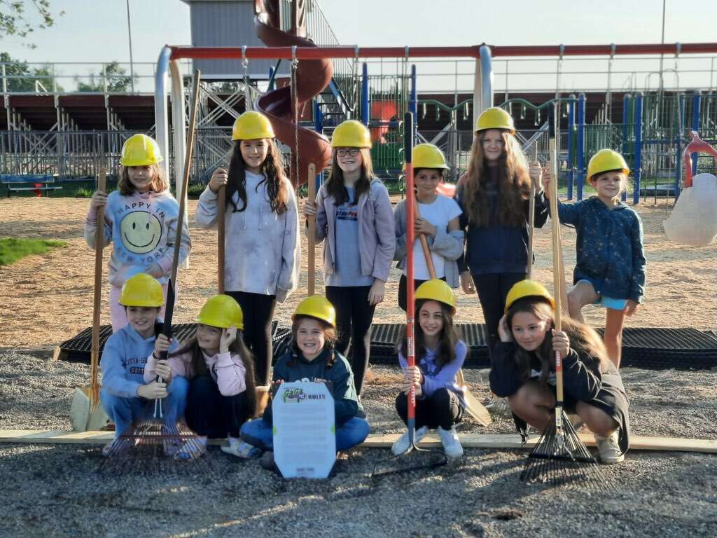 eleven girl scouts wearing yellow hard hats and some are holding shovels