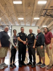 Two PE teachers standing to the left and the right of two police officers in uniform at a gymnasium