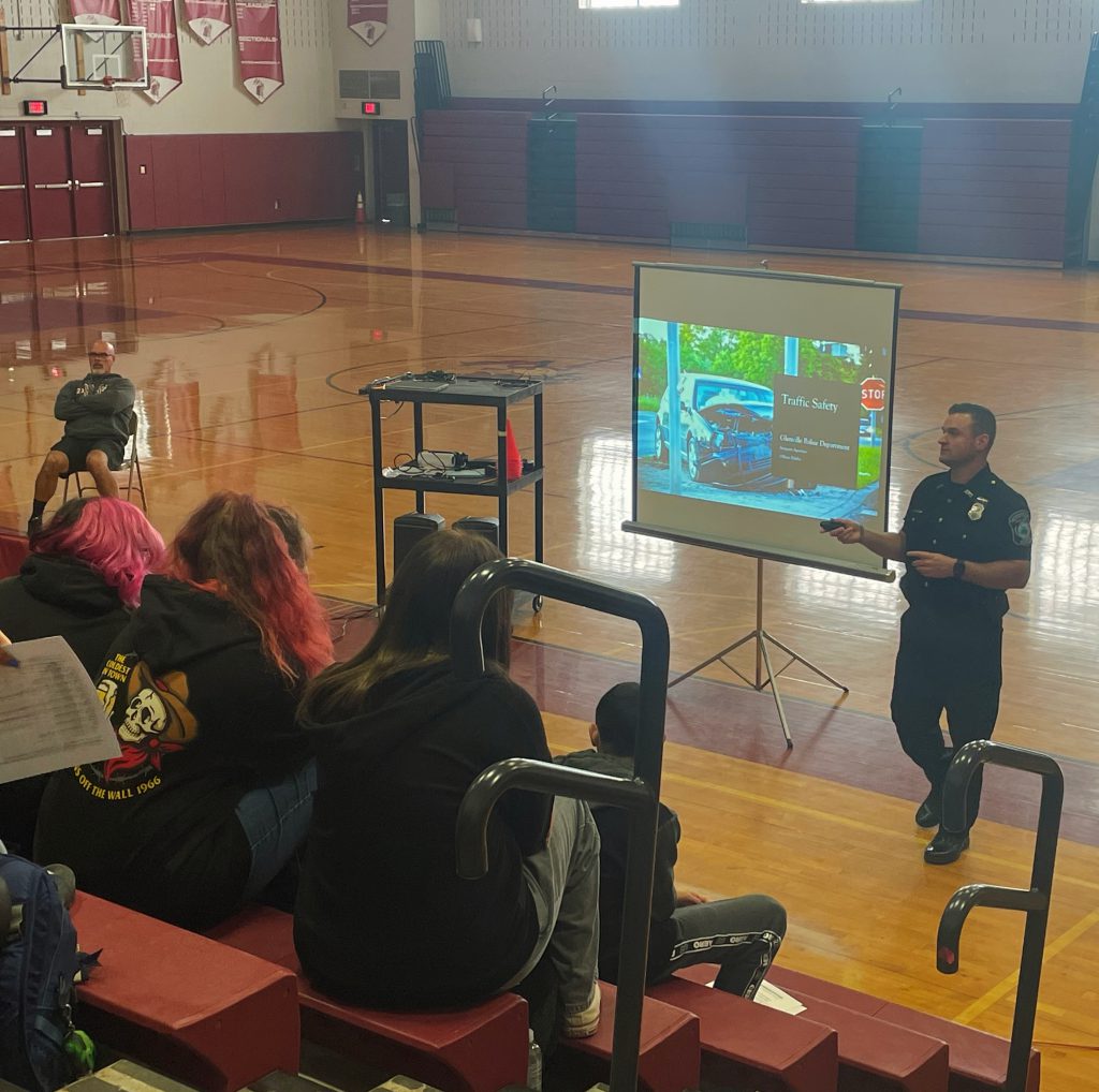 Officer standing on gym floor speaking with students sitting on bleachers