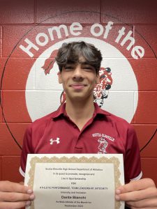 student with short dark hair hair and red polo shirt holds certificate in front of him with two hands