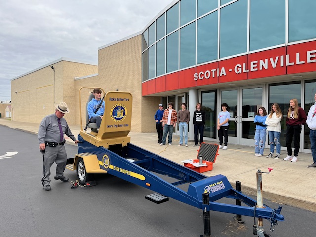 police officer operates a contraption called the convincer as a students sits in the seat ready to slide down ramp