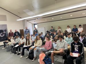 students sitting in chairs listening to a girl in the front row speaking