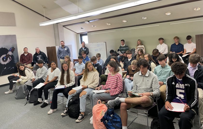 students sitting in chairs listening to a girl in the front row speaking