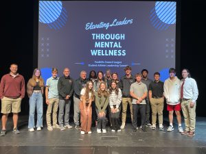 students and coaches standing on stage in front of a sign that says elevating leaders through mental wellness