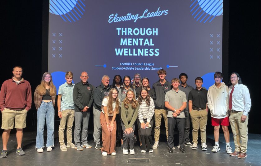 students and coaches standing on stage in front of a sign that says elevating leaders through mental wellness