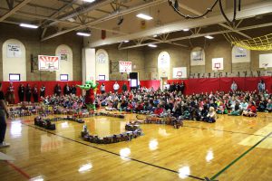 students sitting on gym floor with food they donated in front of them. 