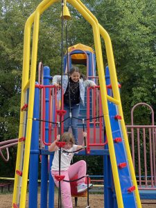 students climb red steps and hold on to yellow poles to reach a yellow bell to ring