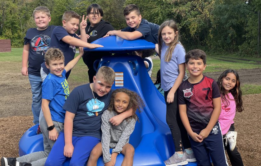 students sitting on and standing around ten spin playground equipment