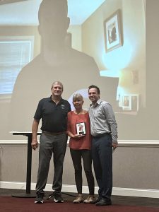 parents and former teammate accepting award with screen of inductee's face behind them