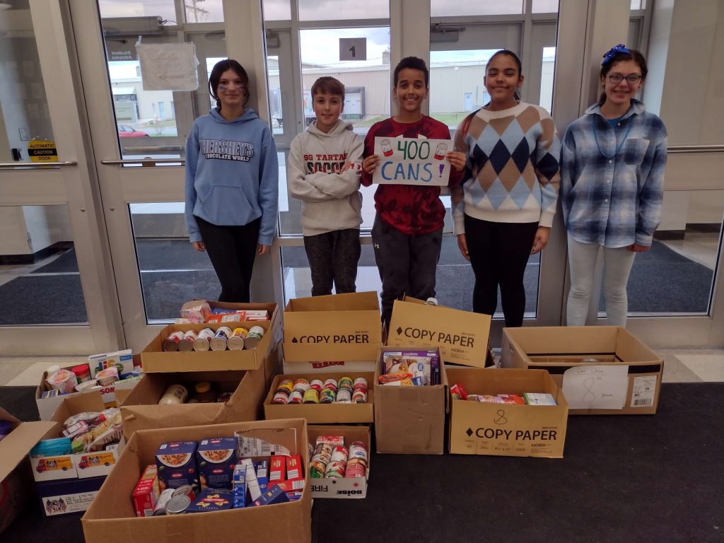 five students standing behind boxes of food they collected. The student in the middle is holding a sign that says 400 cans. 