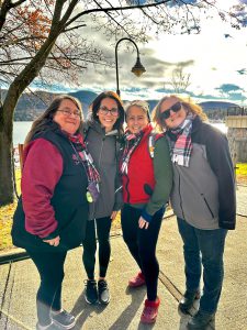 four adults bundled up and standing together with the lake behind them