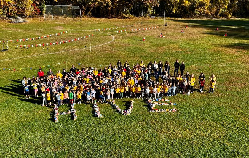 all students and faculty are outside standing on grass with food they collected making the word HIVE