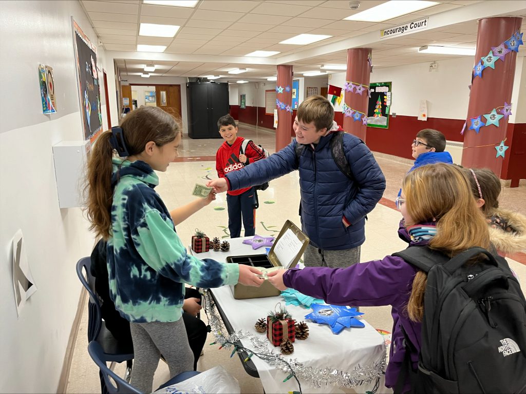 students handing dollars to other students behind a table with Make a Wish stars on them