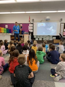 author stands in front of the class holding a pig