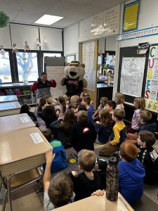 woman sitting next to ValleyCat mascot speaking with children sitting on the ground