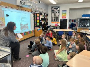 Author sits in a class and reads to students on floor