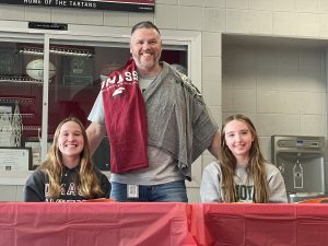 coach proudly standing between two student athletes with a big smile