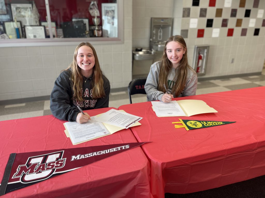 two student athletes sitting at table signing letters to play college sports