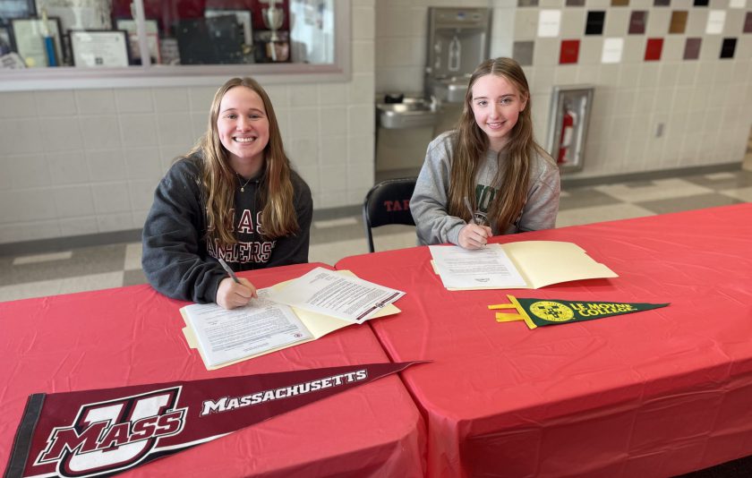 two student athletes sitting at table signing letters to play college sports