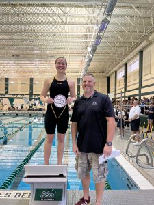 swimmer holding award and coach standing next to pool 