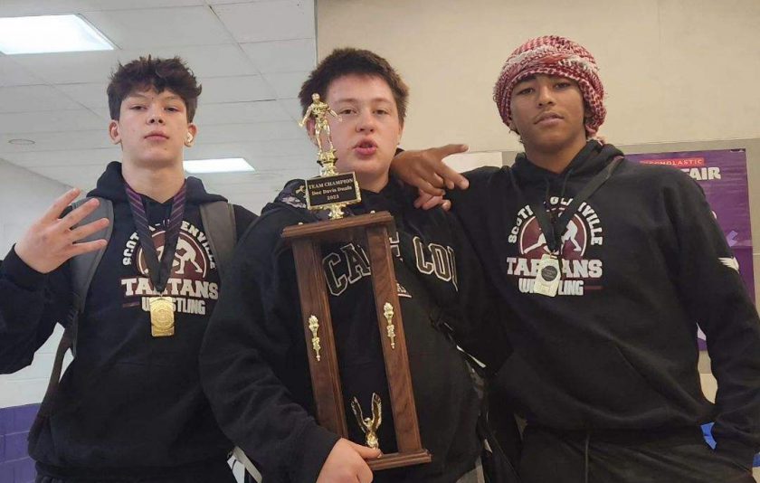 Three wrestlers standing together with their trophy