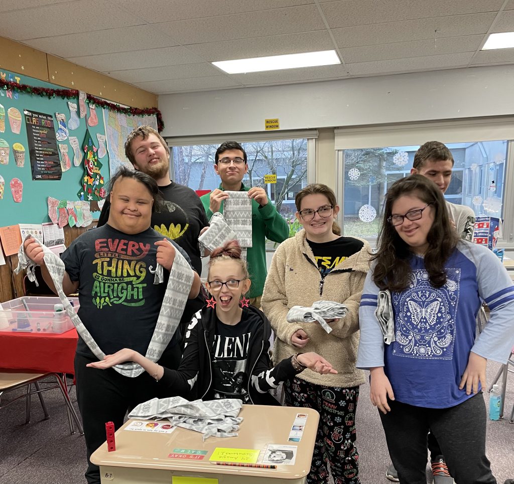 six students standing and one sitting holding scarves that they made.