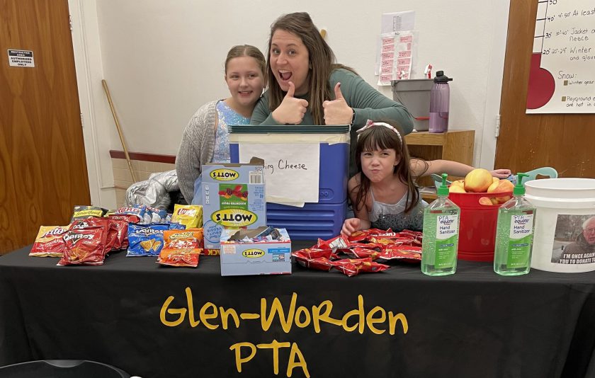 two students and an adult standing behind a table full of snacks