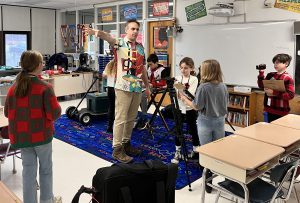 Instructor directing student production crew with clip boards and actors 