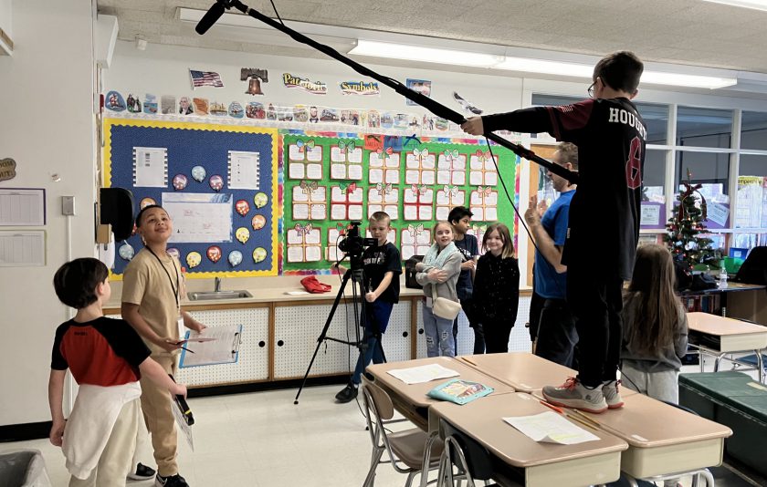 students in classroom making a movie, one is holding a boom mic, others are behind the camera or actors