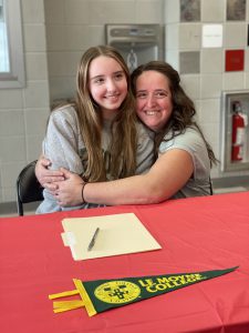 mother hugs daughter from the side with folder on table in front of them