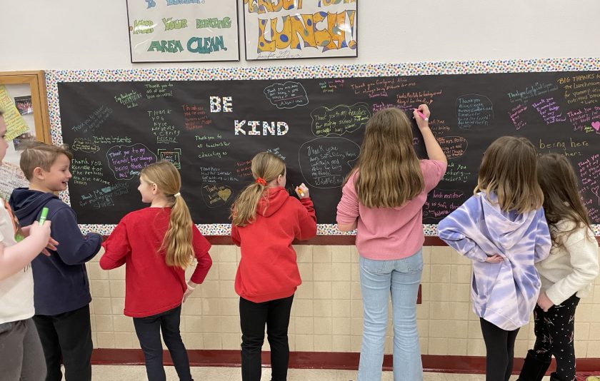 kids writing kind messages on chalkboard