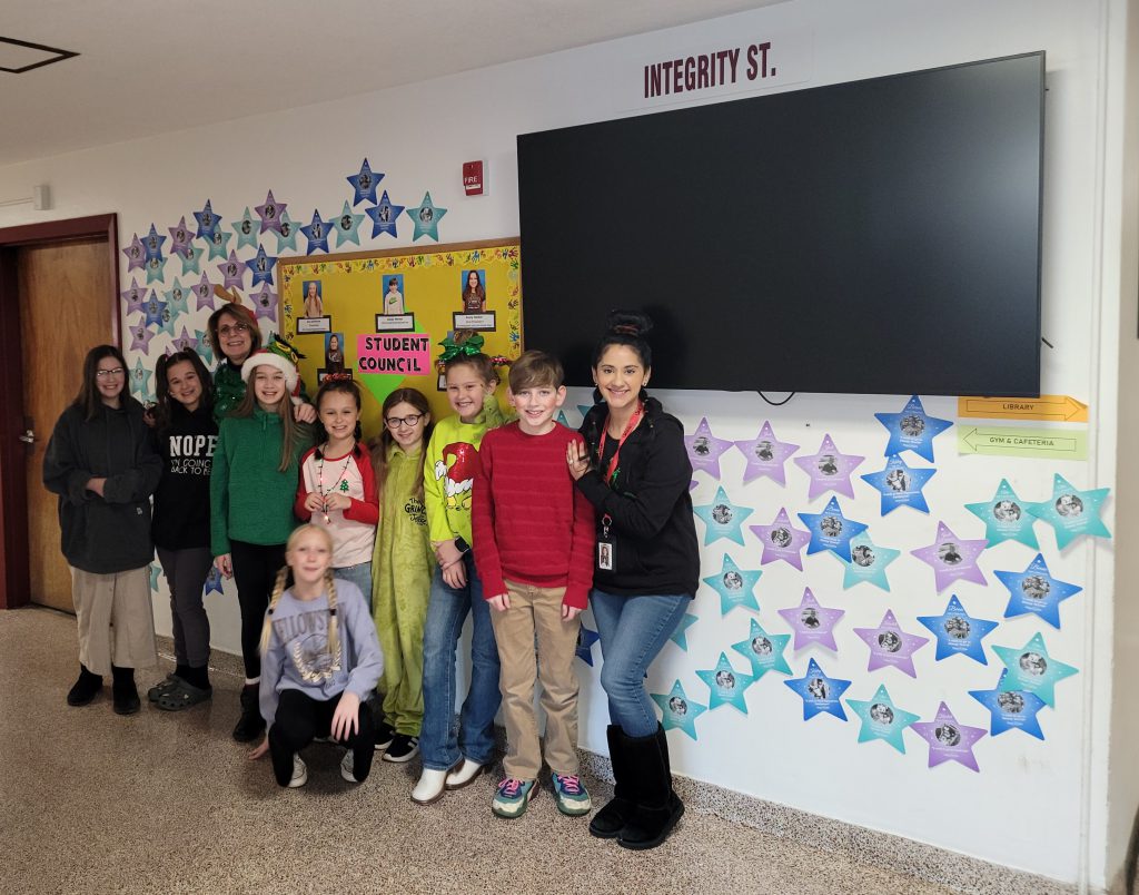 eight student council members and two advisors stand in school hallway next to a wall of stars for Make-A-Wish