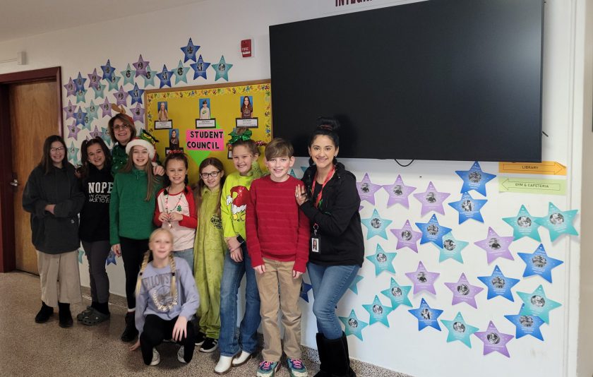 eight student council members and two advisors stand in school hallway next to a wall of stars for Make-A-Wish