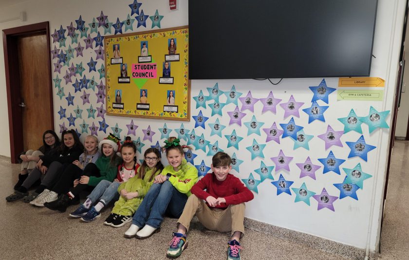eight students sit on the floor in the hallway of school where stars are taped all over the wall.
